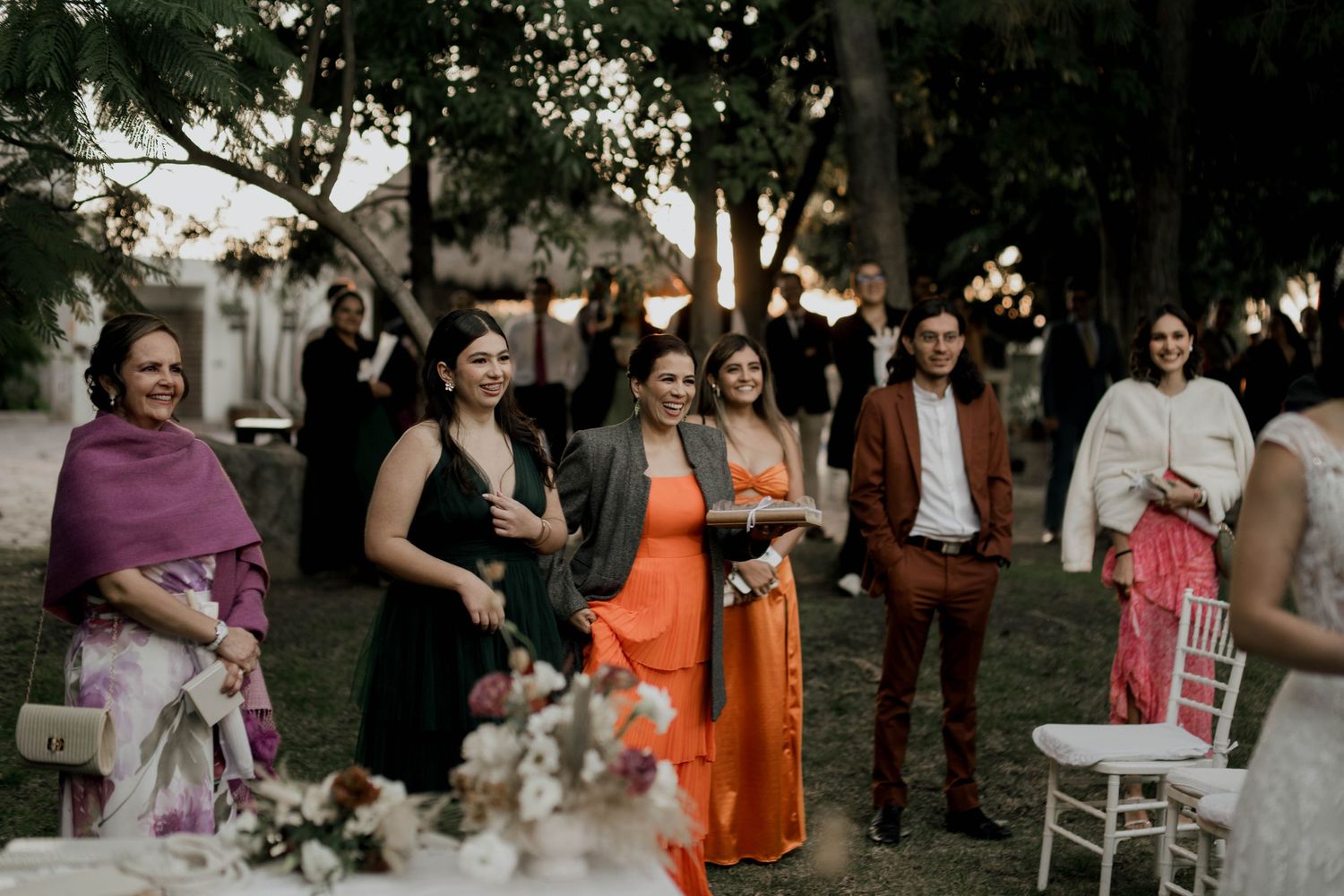 Guests celebrate at an outdoor wedding reception with orange bridesmaid dresses.