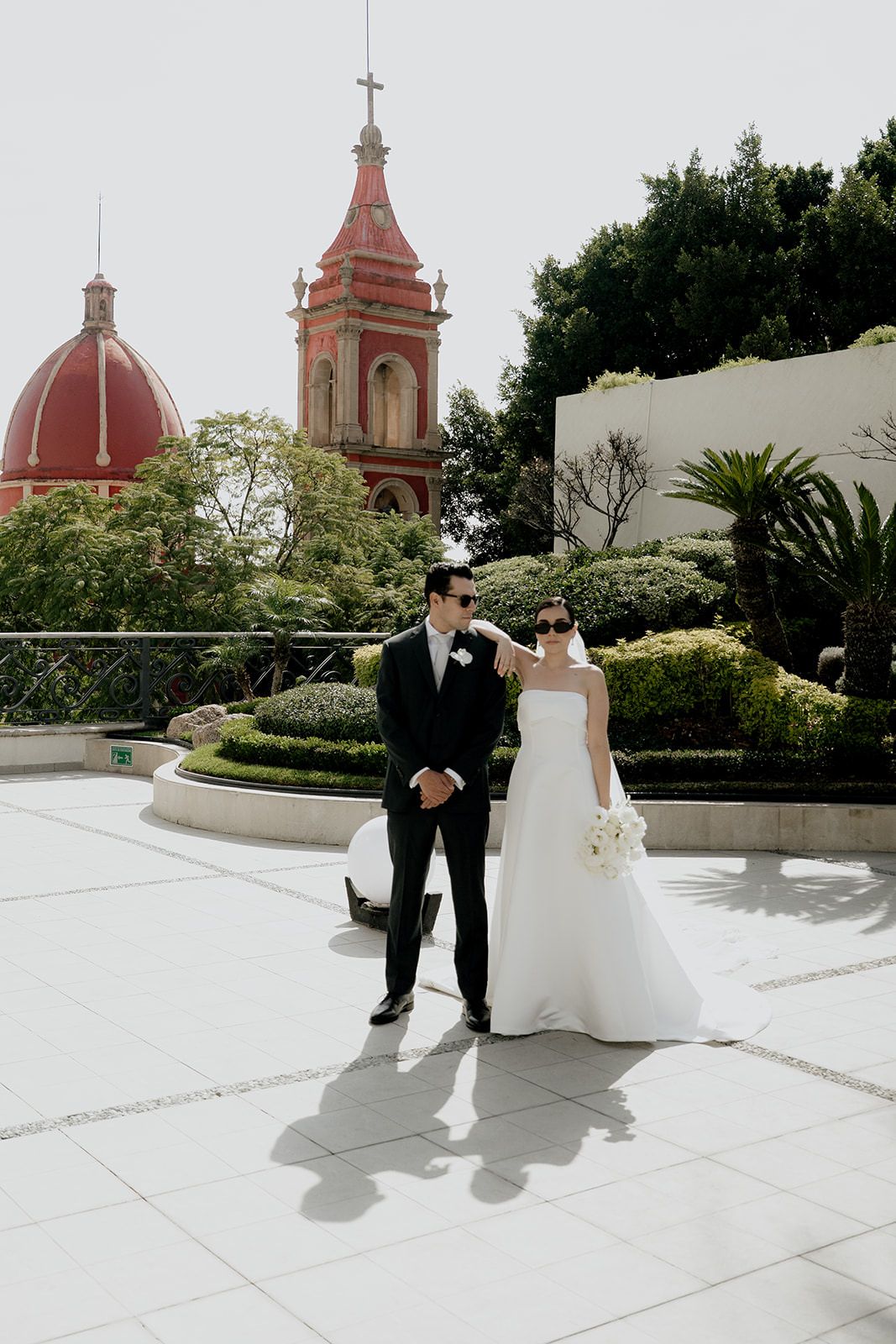 Bride and groom walking on rooftop terrace with stunning red-domed church tower backdrop on sunny wedding day.