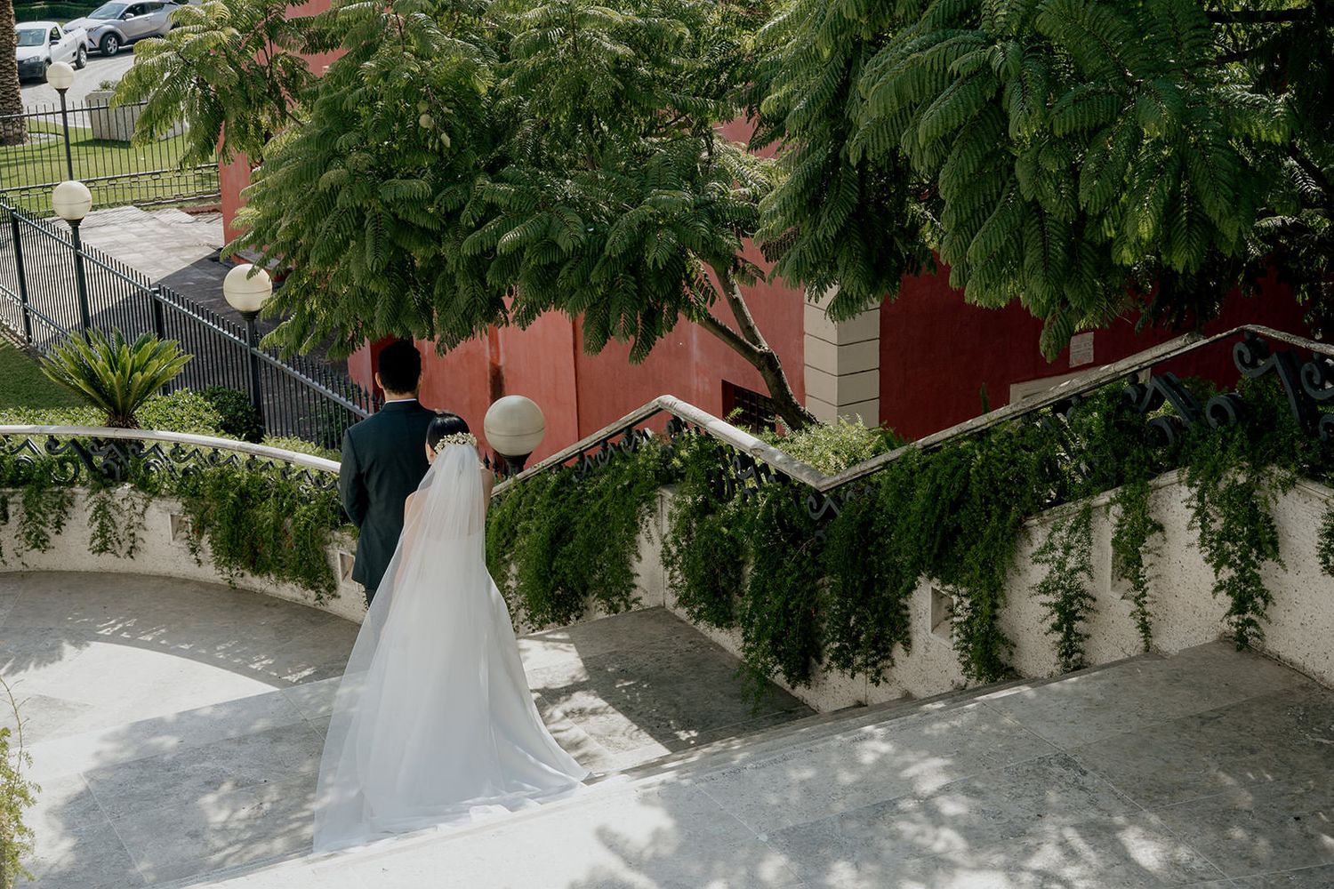 Bride and groom walking up outdoor staircase surrounded by lush green foliage at wedding venue.