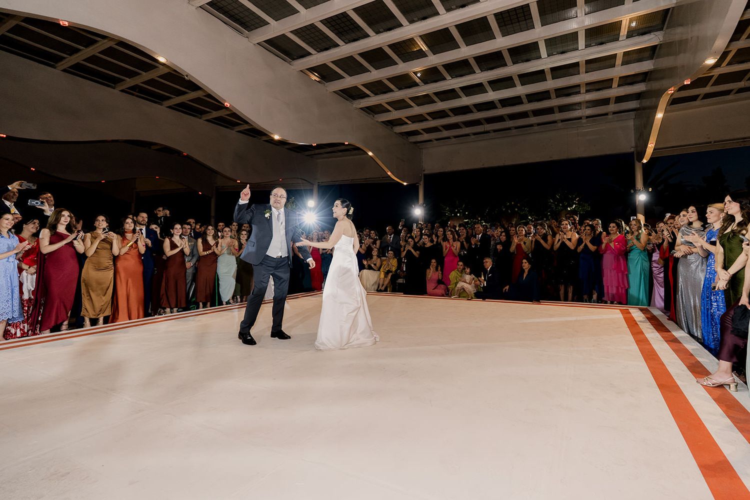 Bride and groom make grand entrance on white dance floor surrounded by cheering wedding guests.