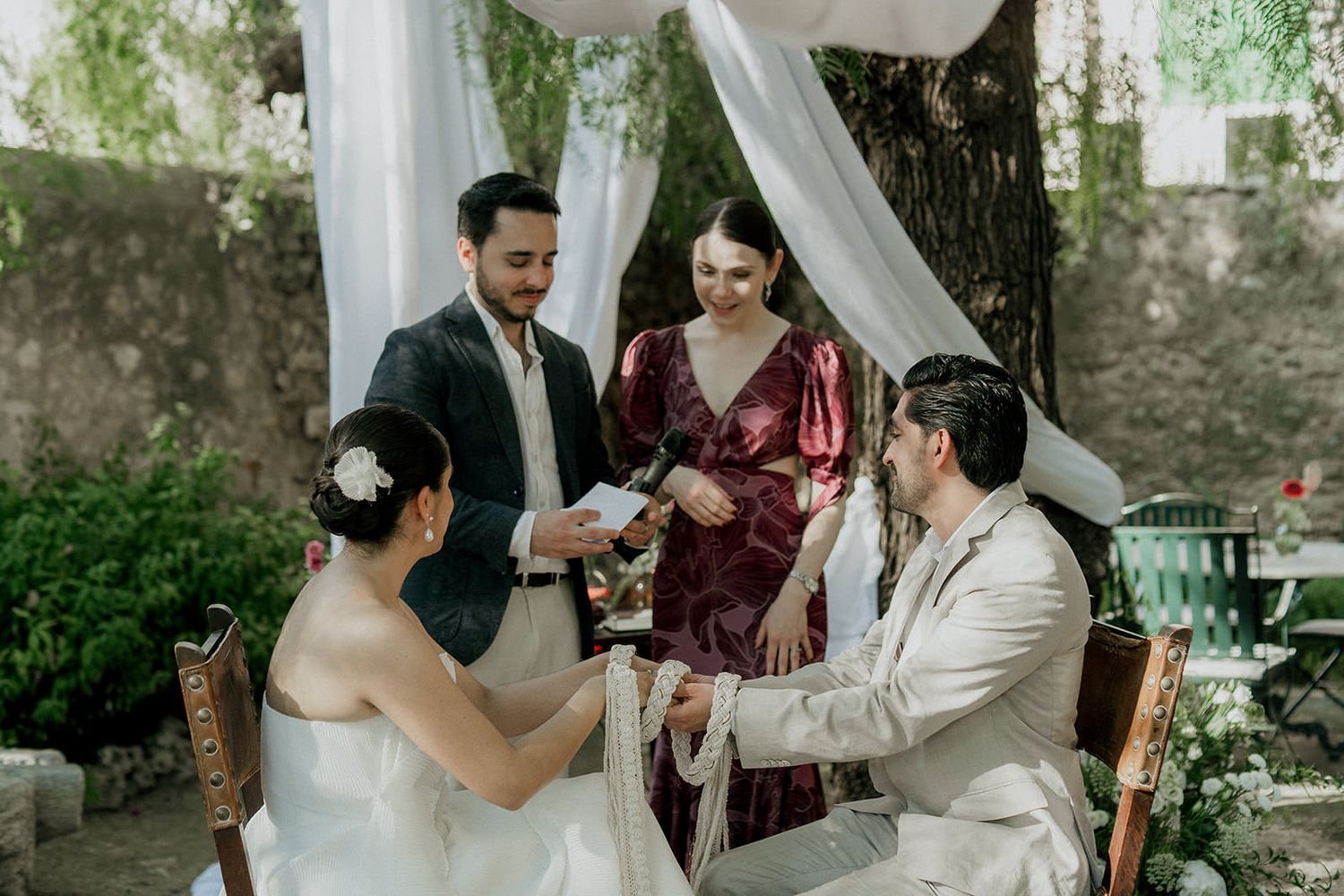 Elegant outdoor wedding ceremony with white drapery and stone architectural details.