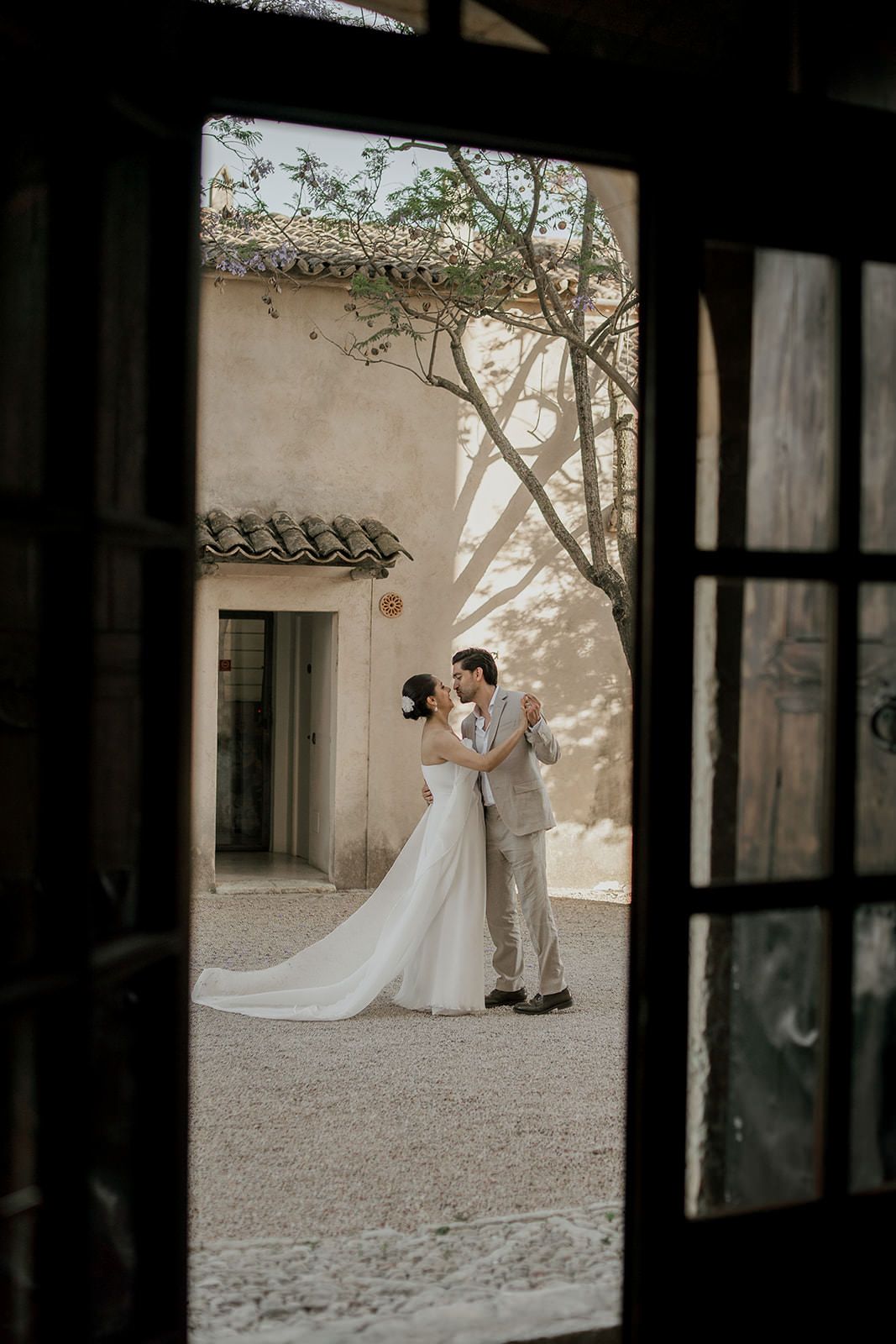 Wedding couple silhouetted through window frames in a rustic courtyard setting.