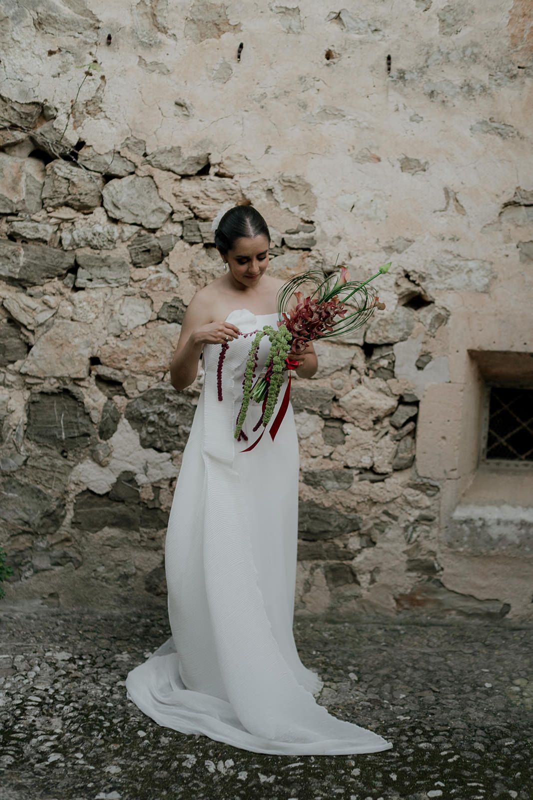 A person in a white dress holding a bouquet against a rustic stone wall.