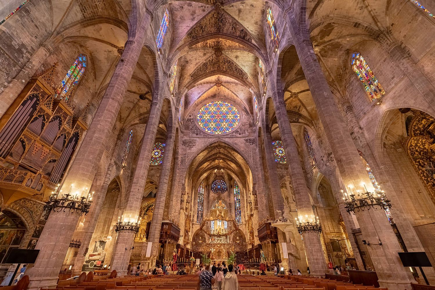 Panoramic view of an ornate baroque church interior with gilded details, vaulted ceilings, and crystal chandeliers.