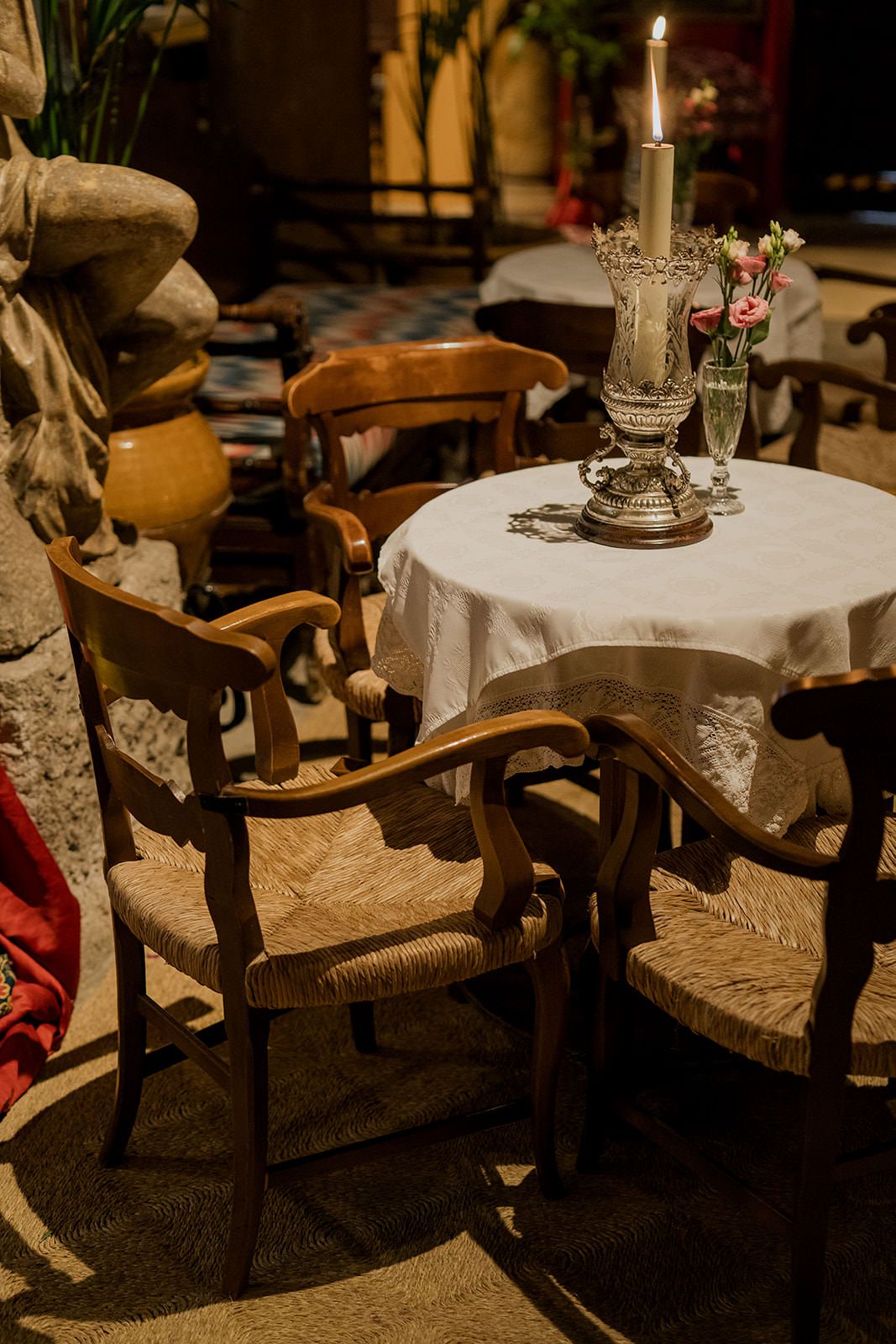 Vintage wooden chairs with woven seats arranged around small round tables with white tablecloths and candlesticks.