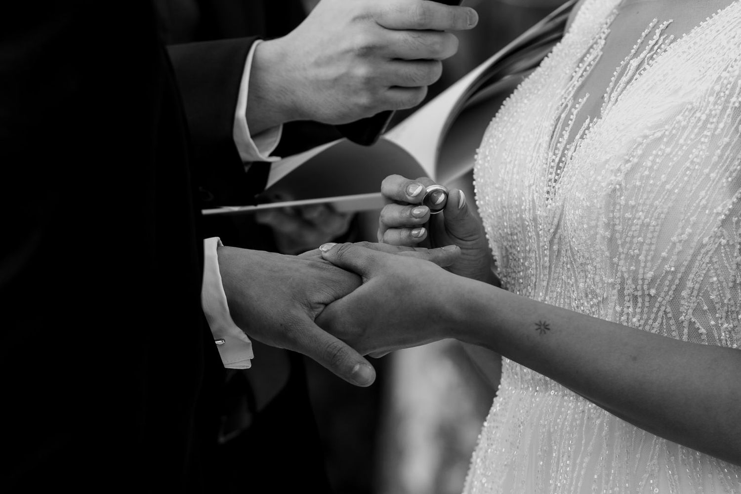 Black and white close-up of bride and groom exchanging rings during wedding ceremony.