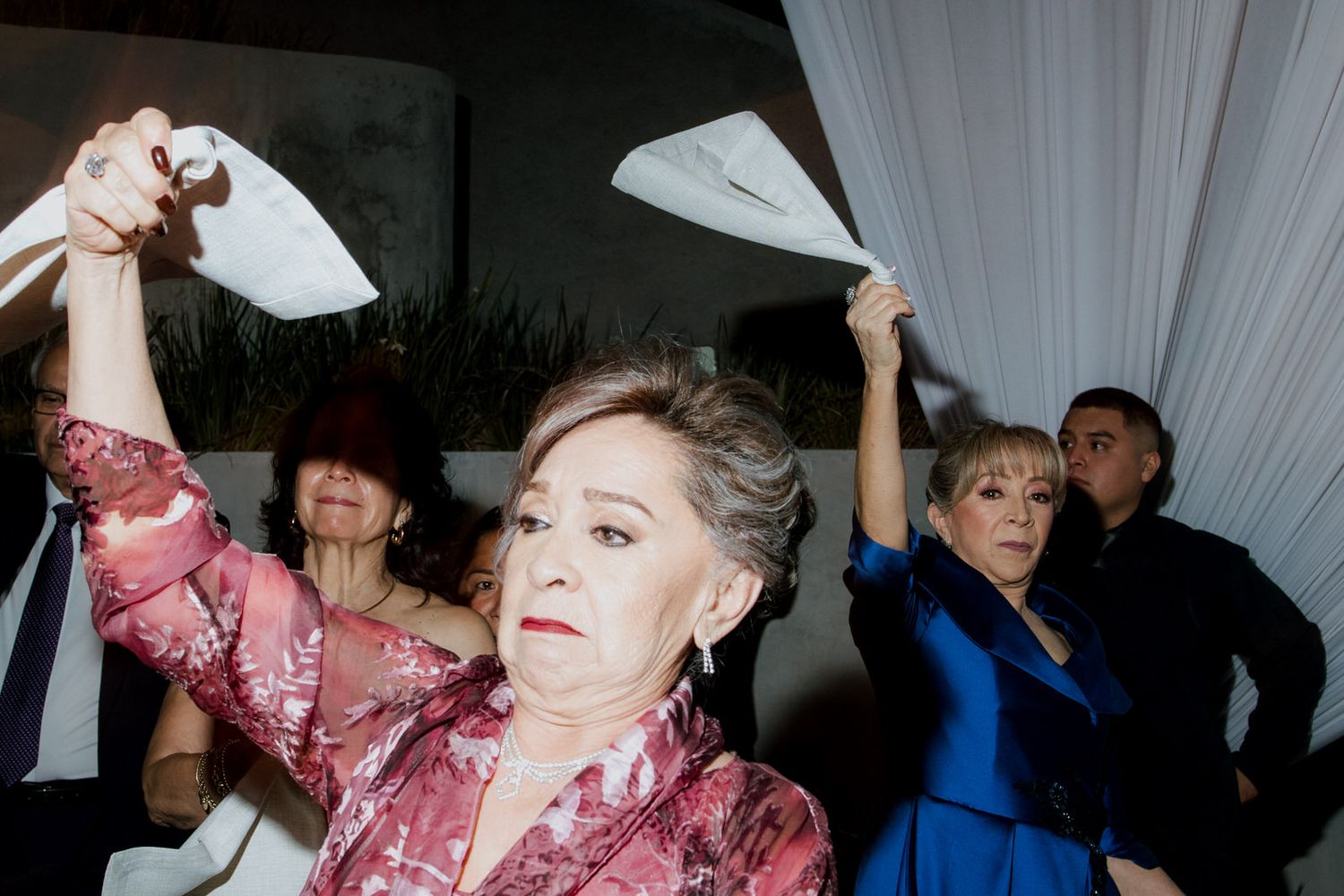 Guests waving white napkins in celebration at a lively wedding reception indoors.