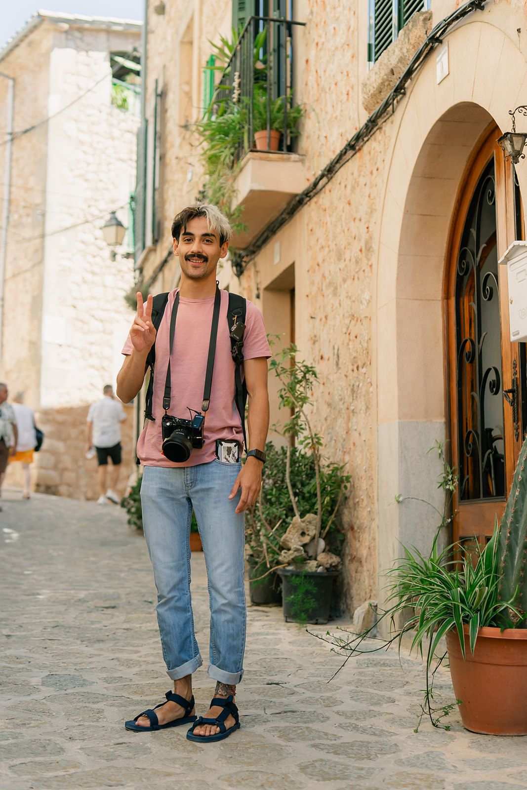 Tourist with camera and sandals exploring charming stone alleyways in a Mediterranean village.