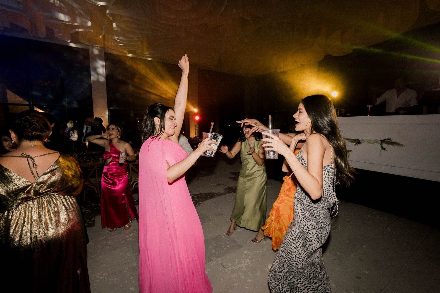 People dancing and mingling at an indoor celebration with ambient lighting.