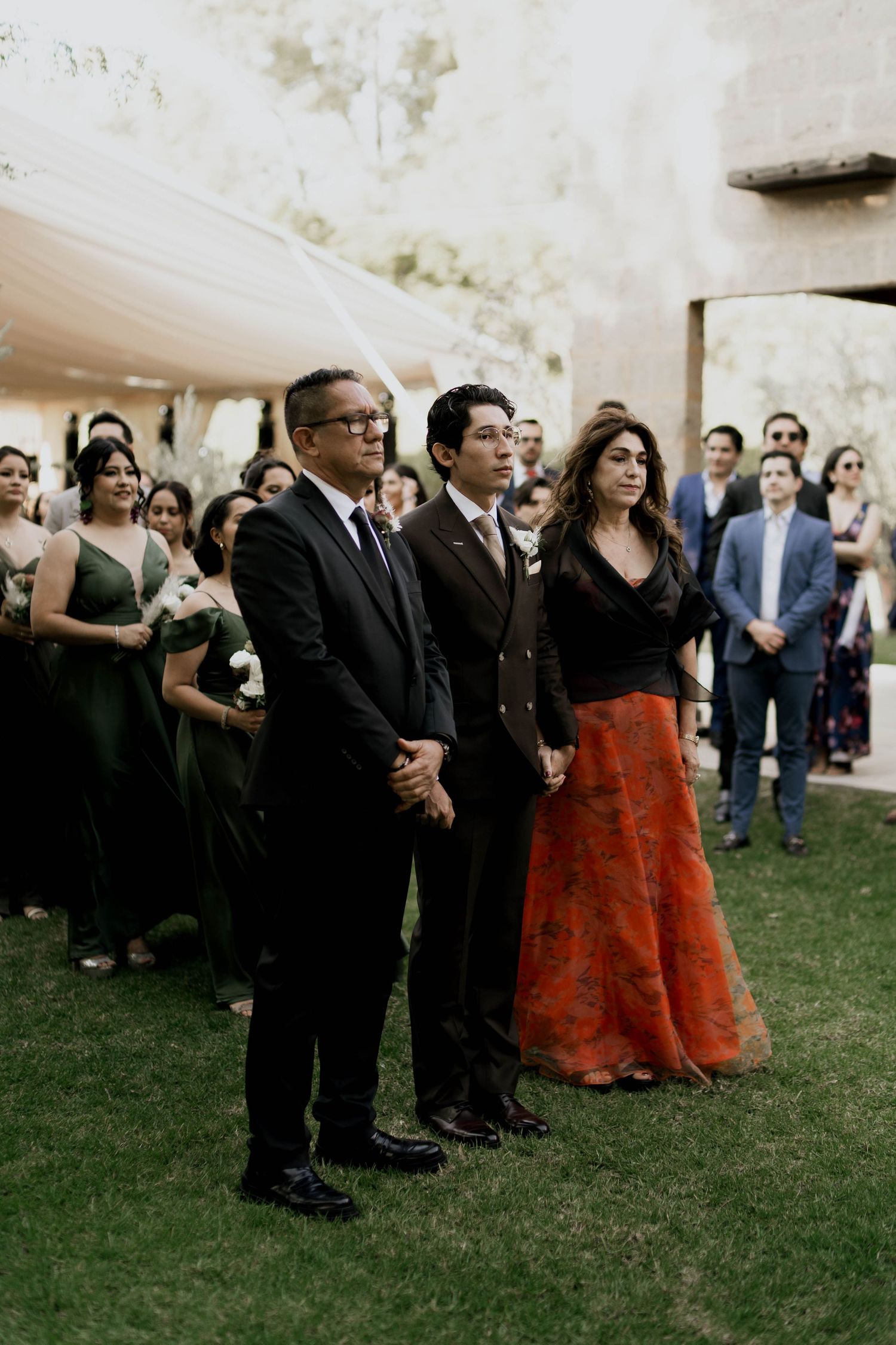 Wedding guests in formal attire standing together during an outdoor ceremony.