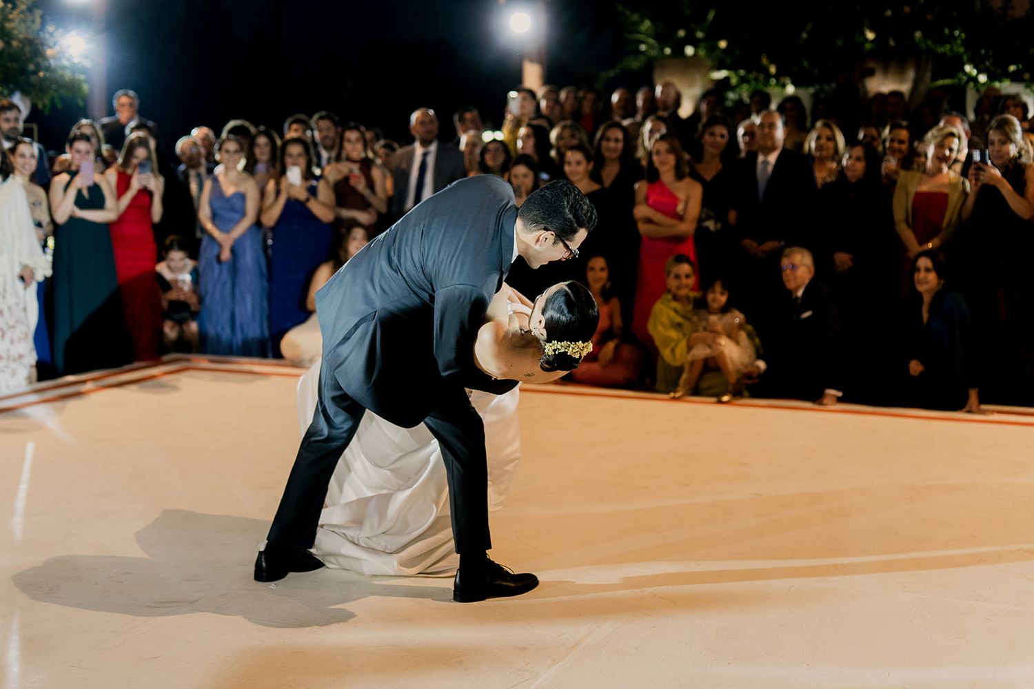 Groom dips bride during first dance at elegant outdoor wedding reception.