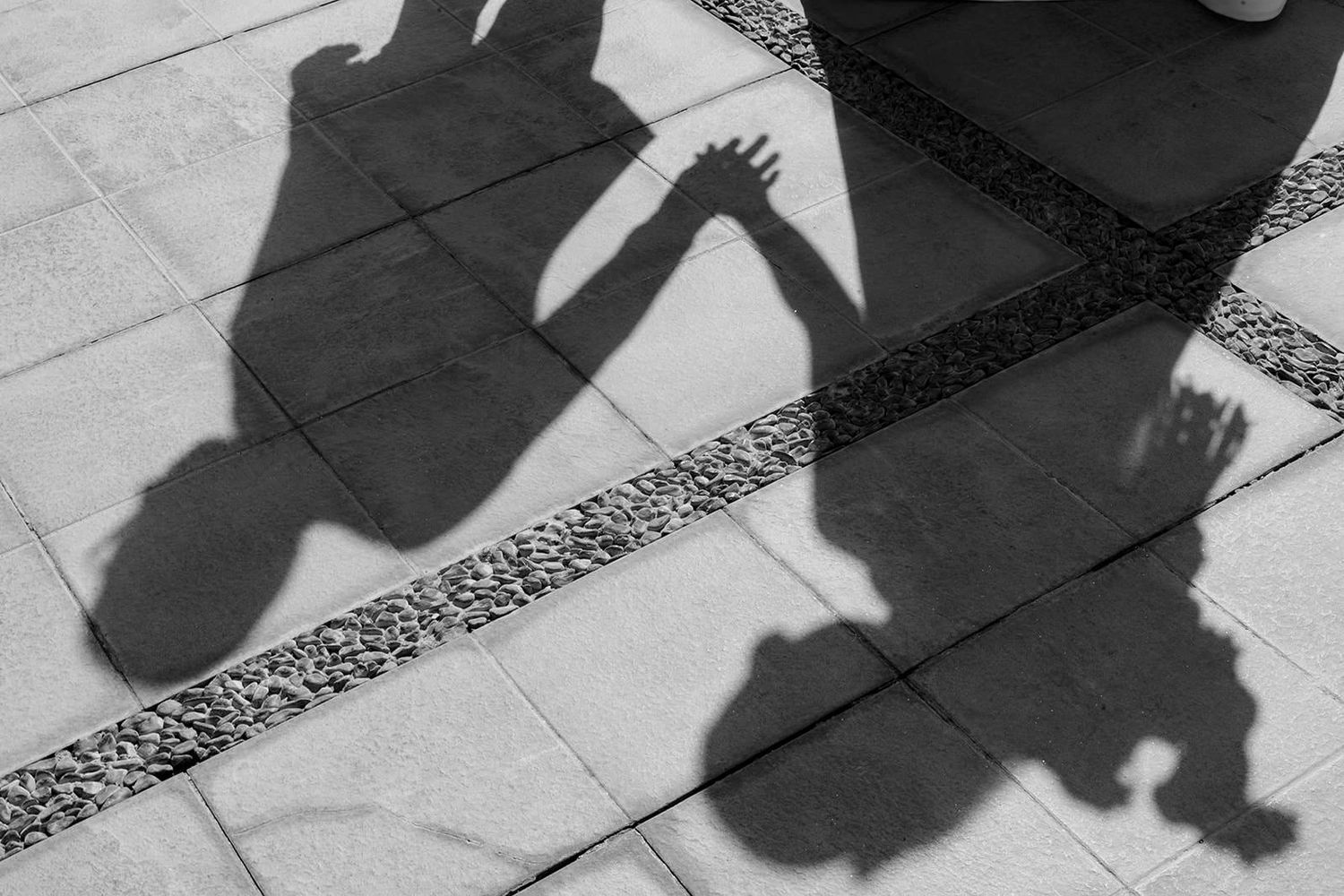 Artistic black and white shadow silhouette of a couple holding hands on a tiled outdoor surface.