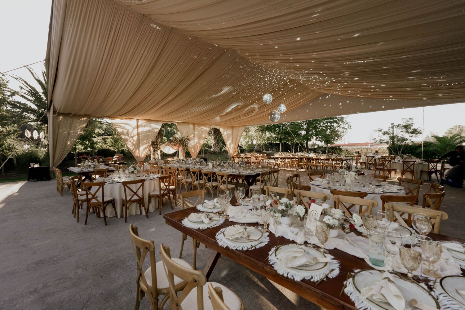 Wedding reception venue with rustic wooden chairs and white tablecloths under draped ceiling.