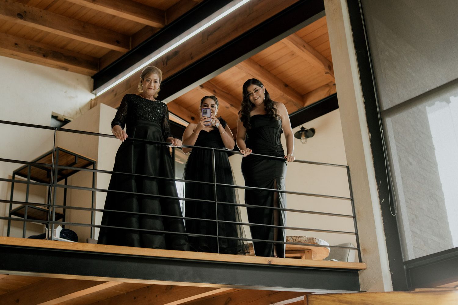 Wedding party poses on a rustic wooden balcony overlooking an indoor venue.