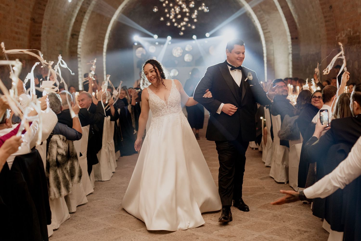 Wedding celebration with guests dancing and cheering in a dramatically lit brick tunnel venue.