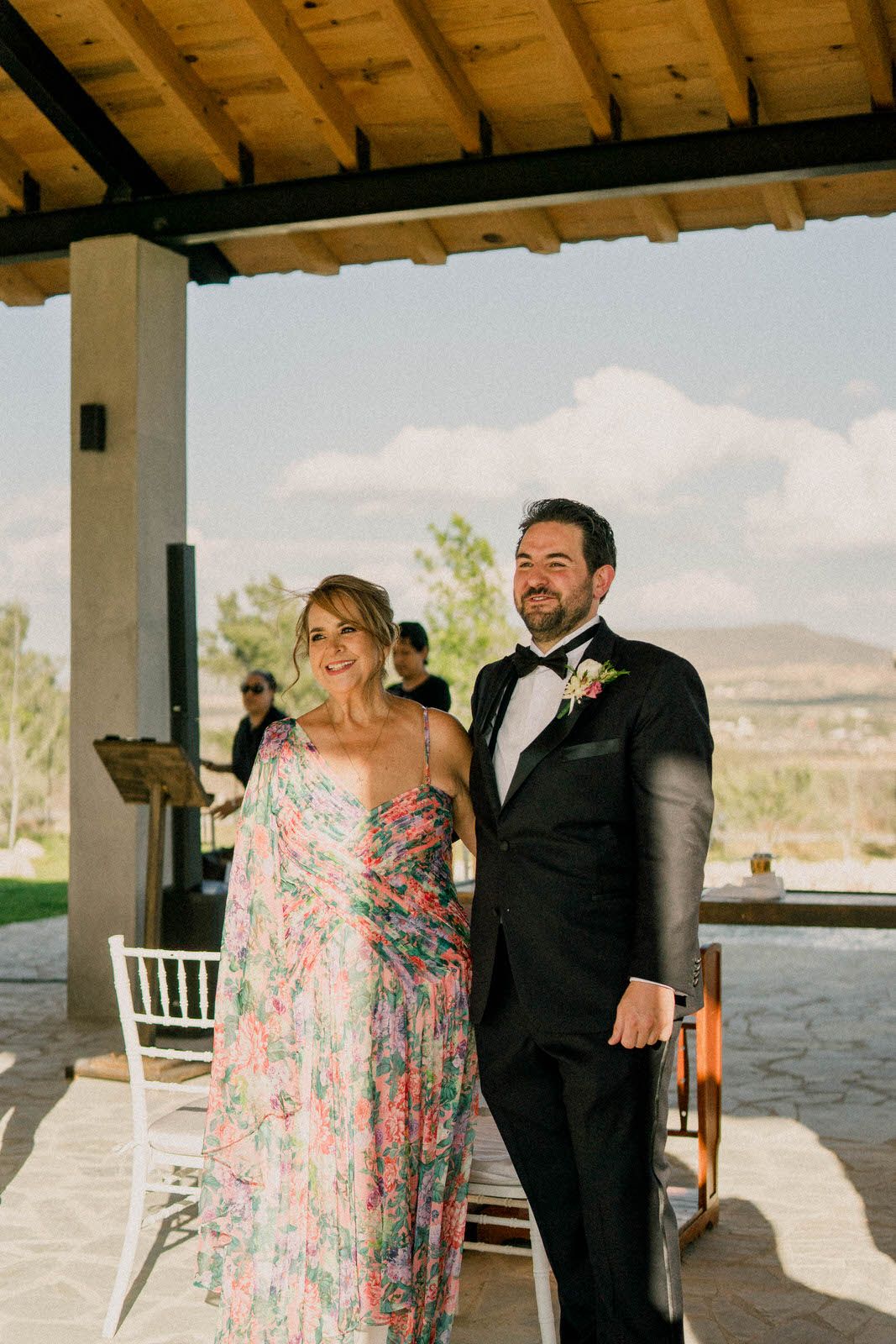 Wedding celebration under wooden beams with mountain scenery in background.