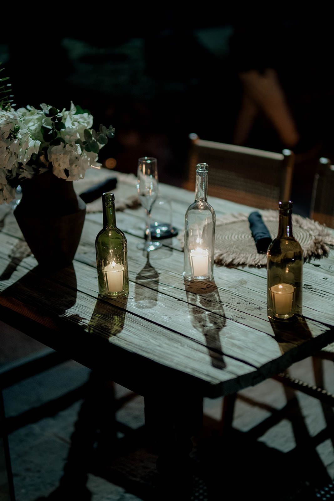 Rustic table setting with wine bottles and candles creating ambient lighting.