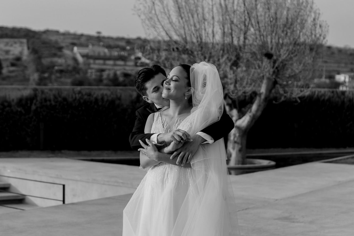 Black and white photo of a bride and groom embracing outdoors on their wedding day.