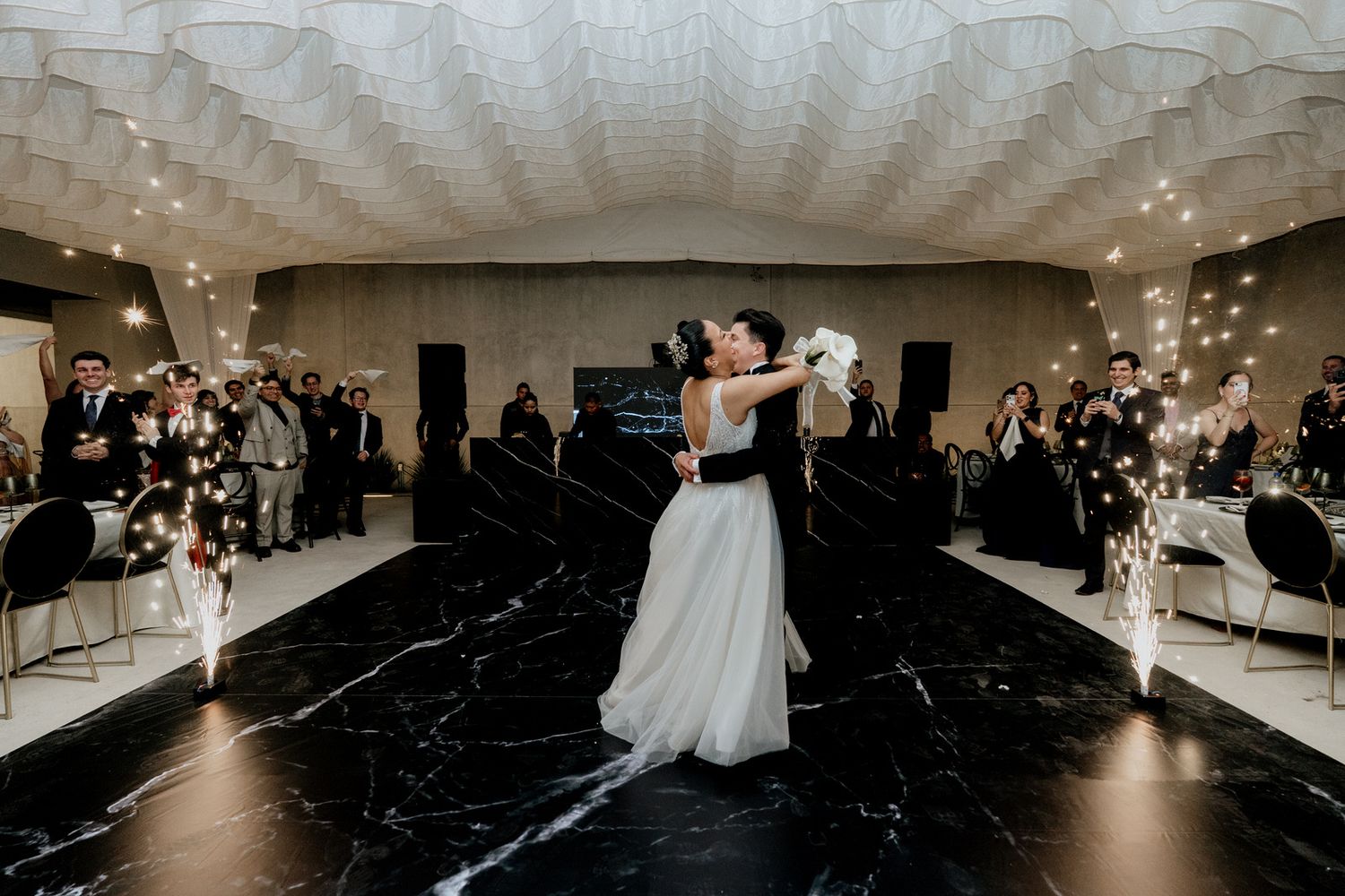 Bride and groom share first dance on black marble floor in elegant wedding reception venue with sparklers.