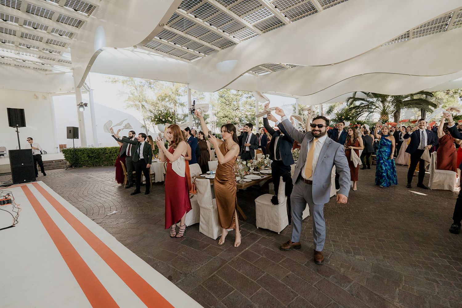 Wedding guests raise their hands in celebration on the dance floor at an outdoor reception.