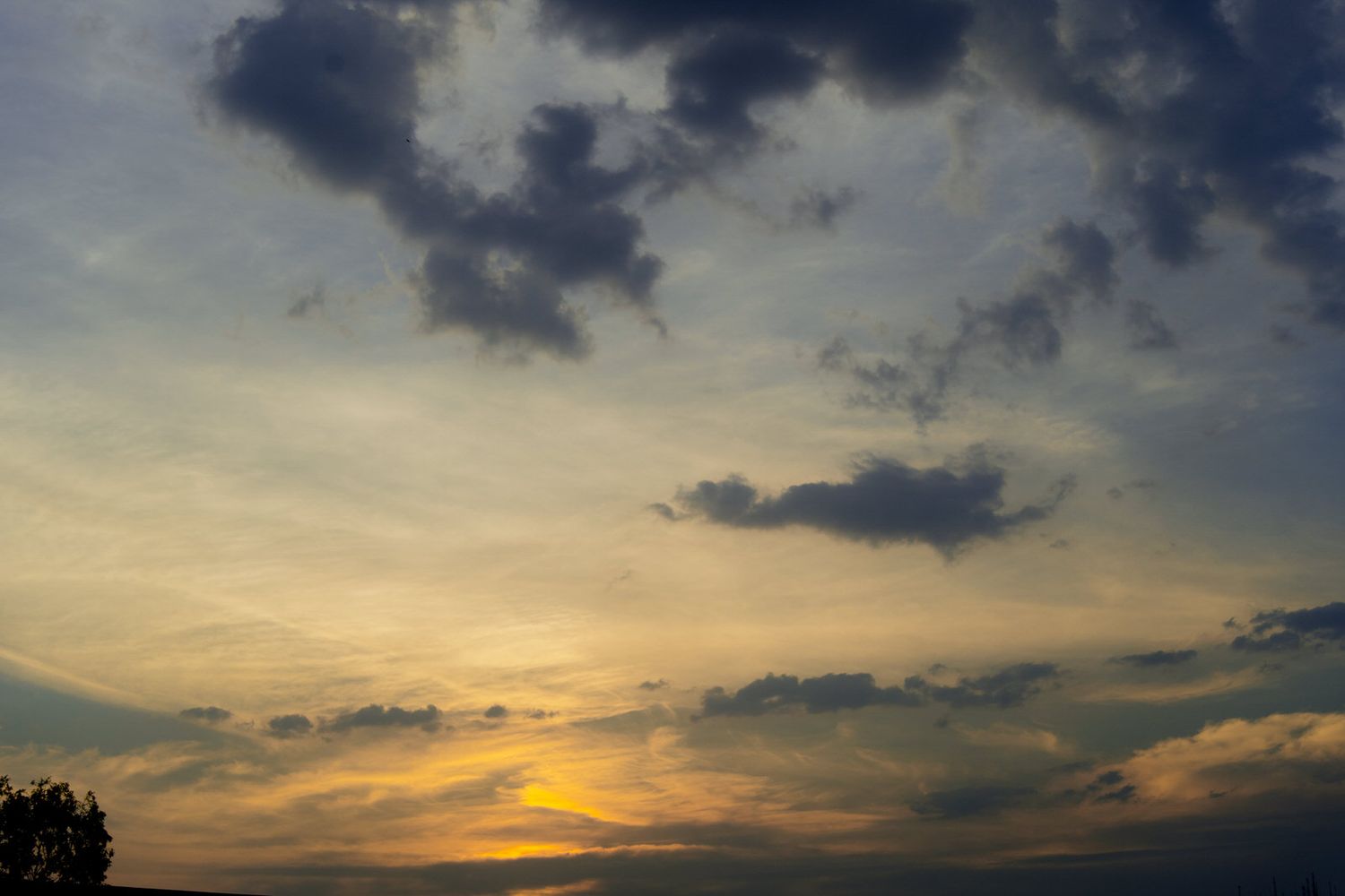 Golden sunset sky with dramatic dark clouds creates stunning backdrop for outdoor wedding venue.