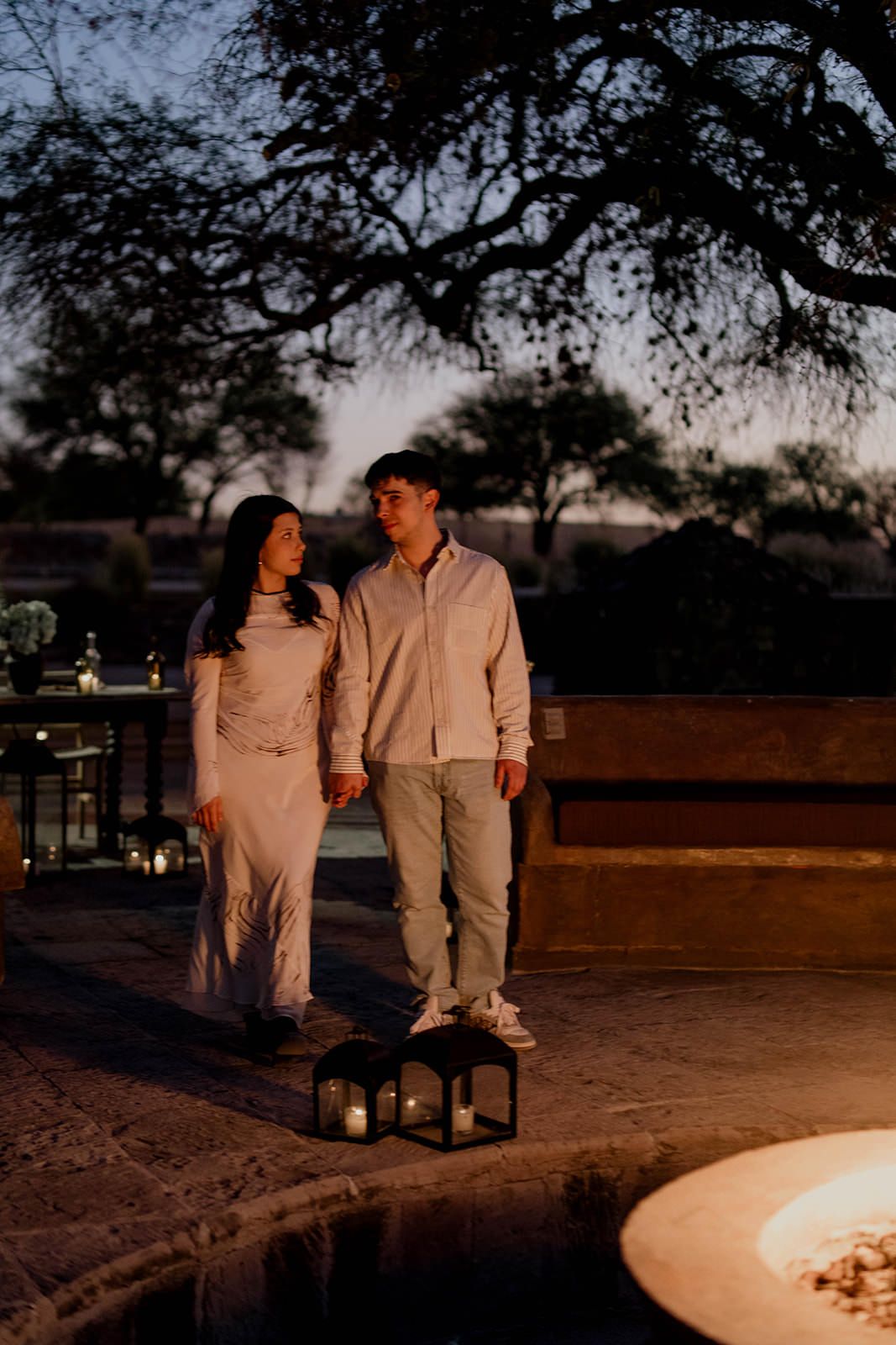 Couple in white clothing share an intimate moment at sunset near decorative lanterns.