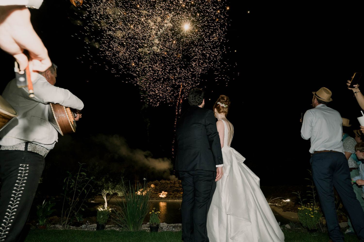 Sparklers create magical light trails against the dark night sky at an outdoor wedding celebration.