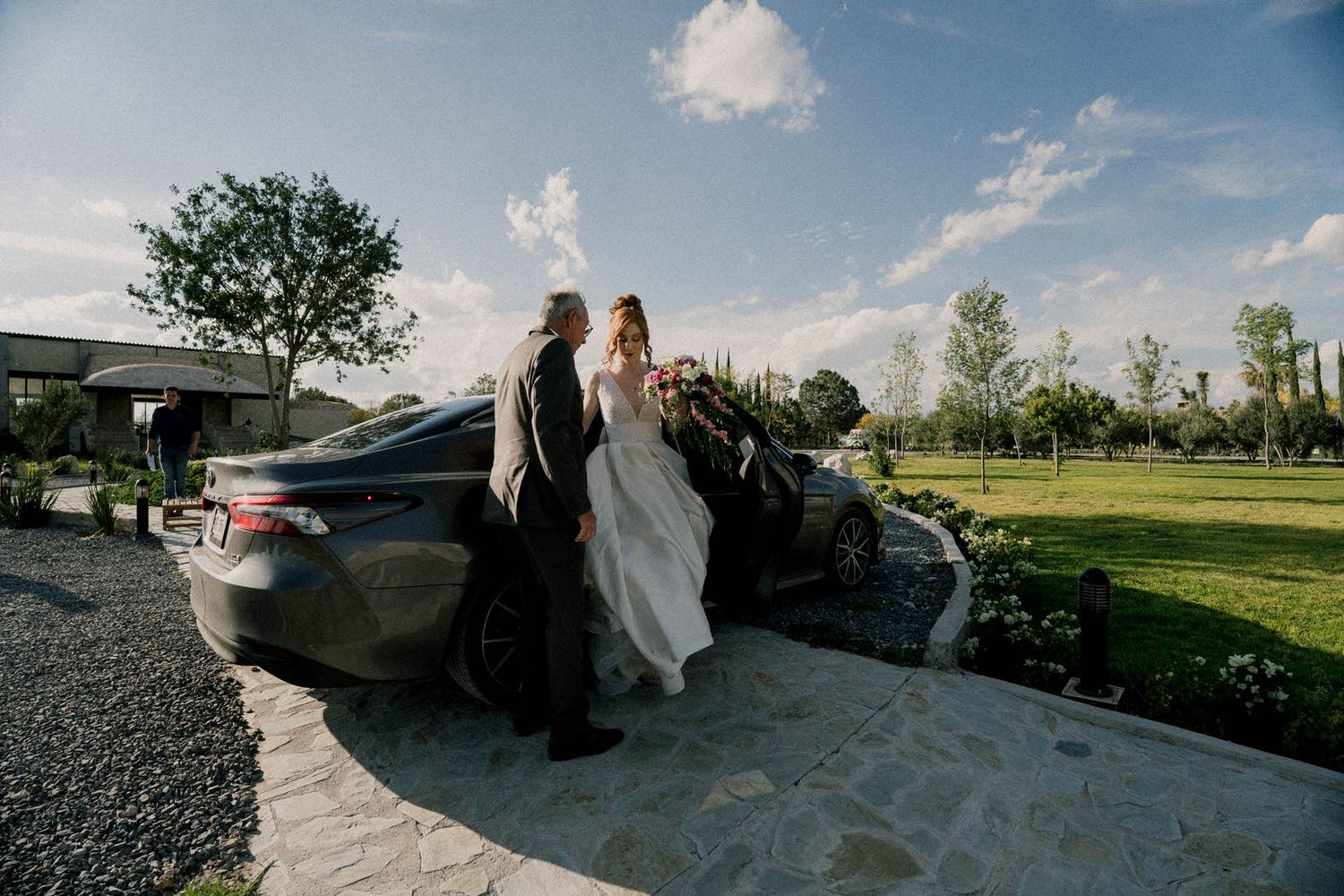 Wedding party gathering near parked vehicles at scenic outdoor venue.