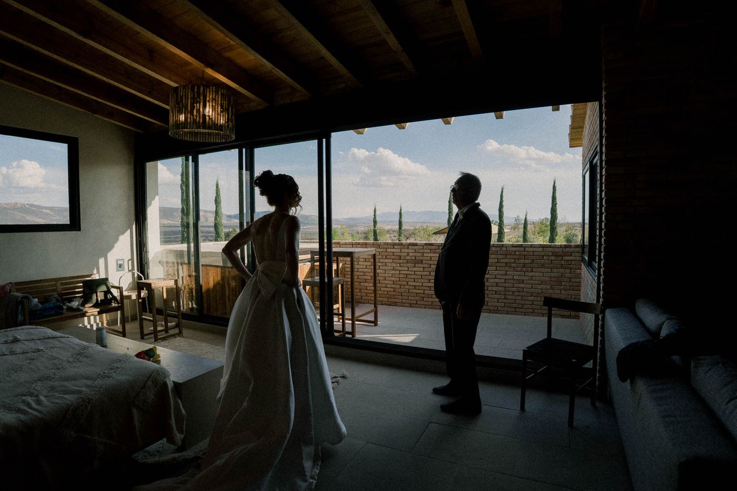 Silhouetted figures in a dark room with large windows overlooking a landscape.