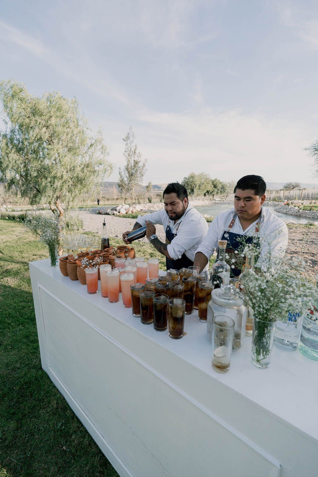 Long white bar counter with various cocktails and drinks displayed outdoors.