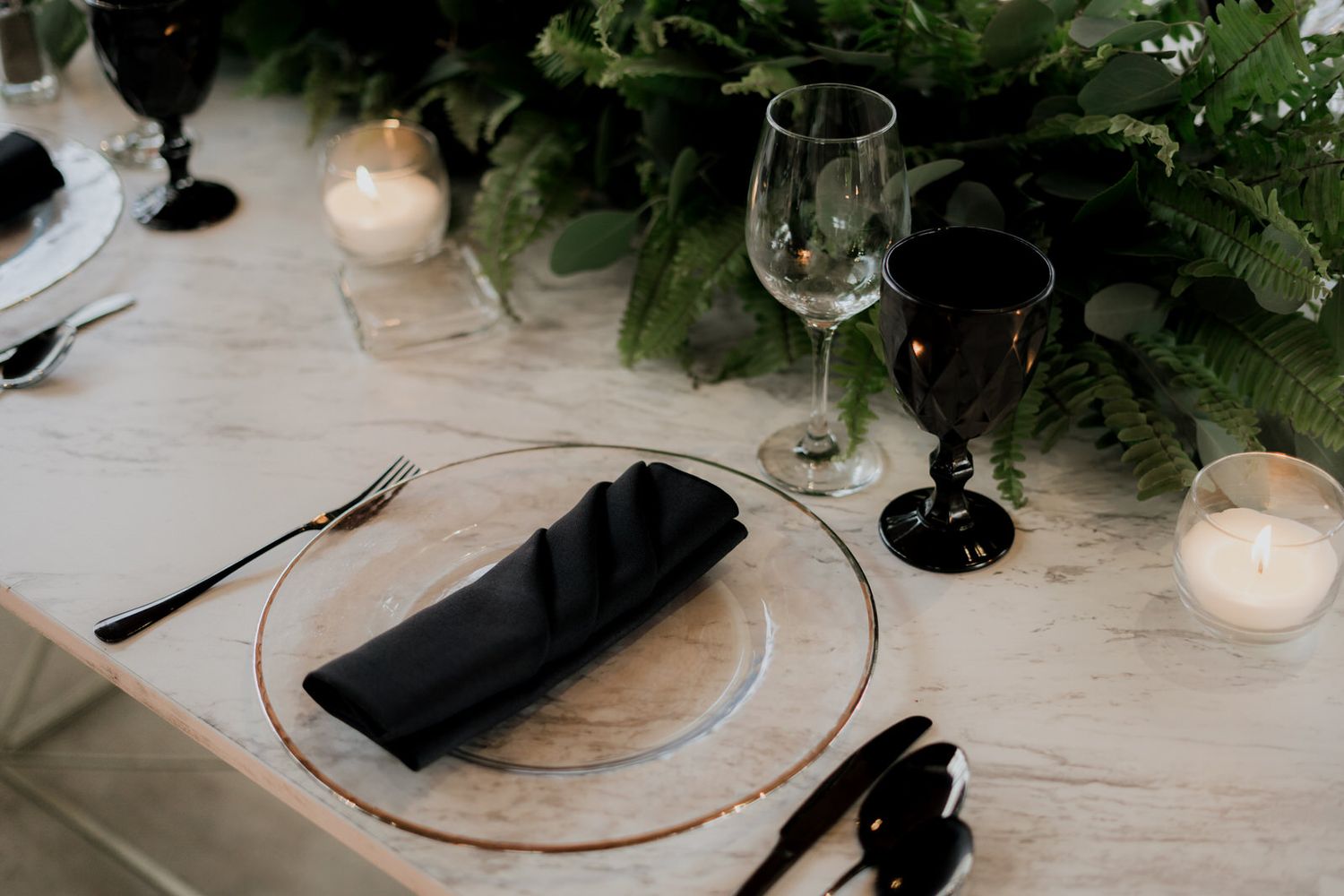 Elegant table settings with black napkins, crystal glasses, and greenery decorations.