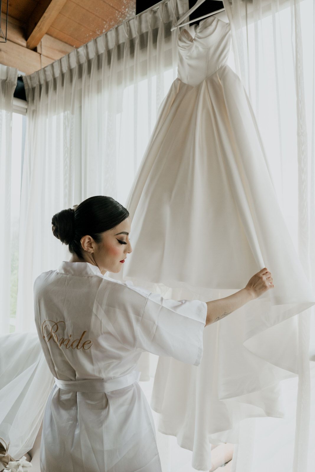 Wedding preparation scene with white dress being arranged in sunlit room.