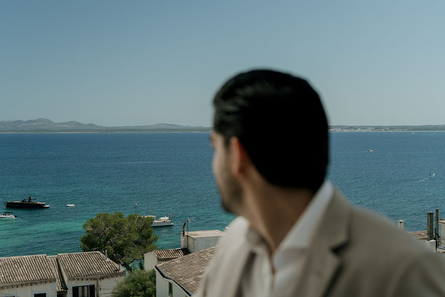 Person in a blazer gazes at the turquoise Mediterranean Sea from a coastal viewpoint on a sunny day.