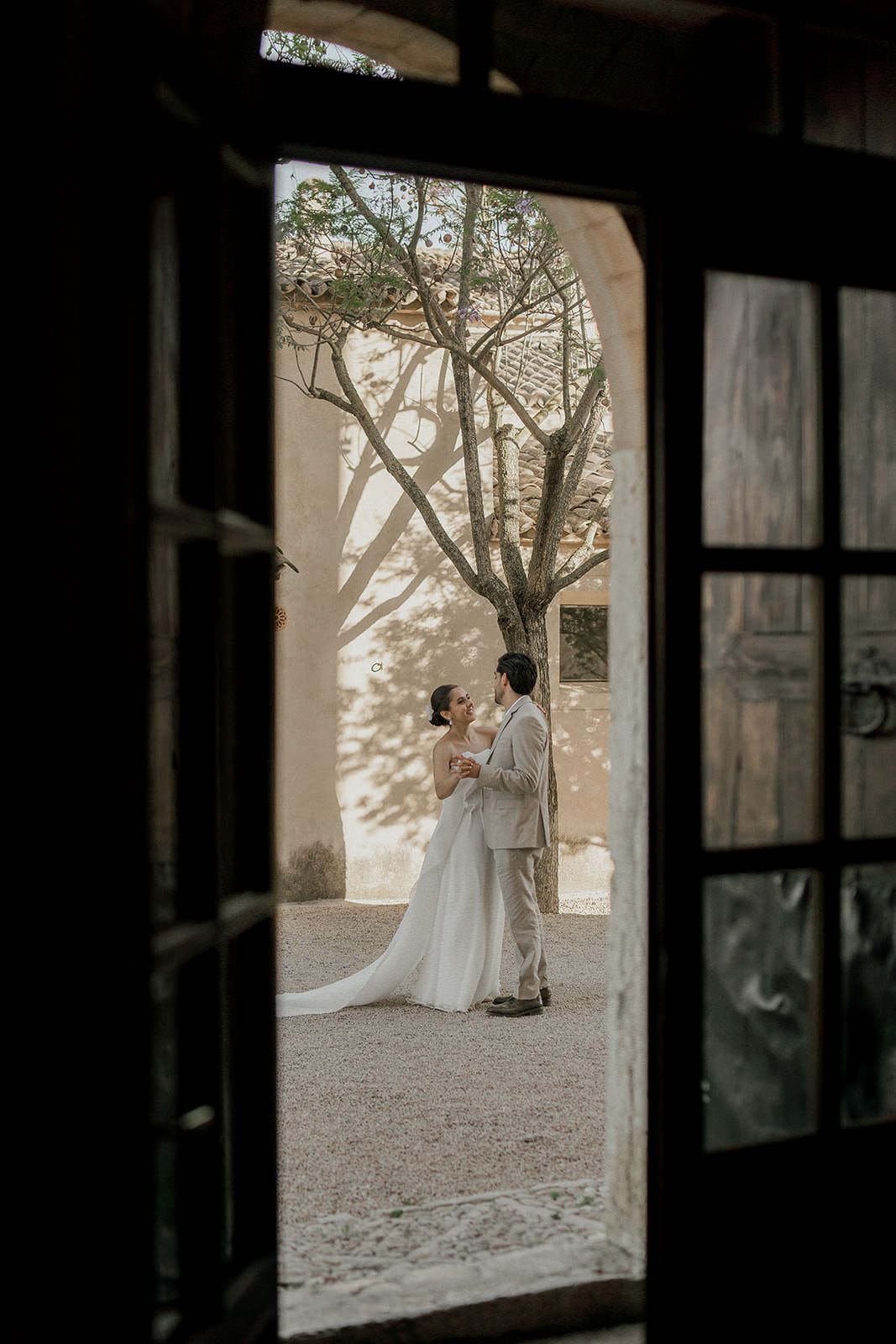 A wedding couple silhouetted through a window frame in a romantic outdoor setting.