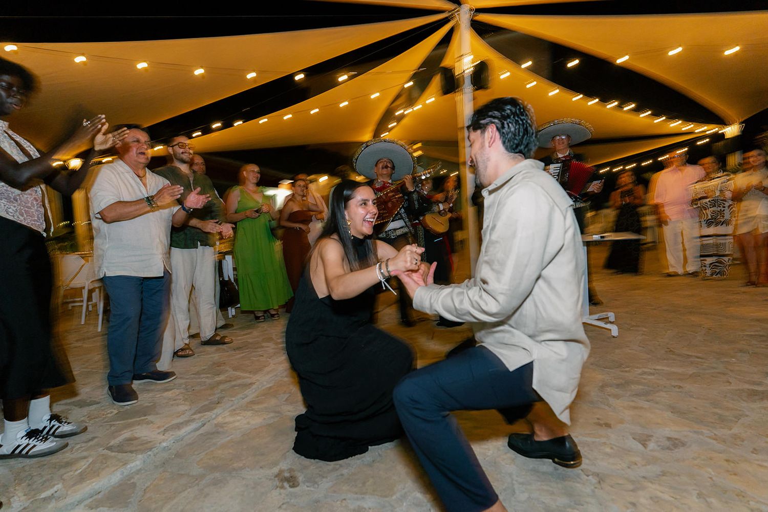 People dancing and having fun at an indoor event with string lights overhead.