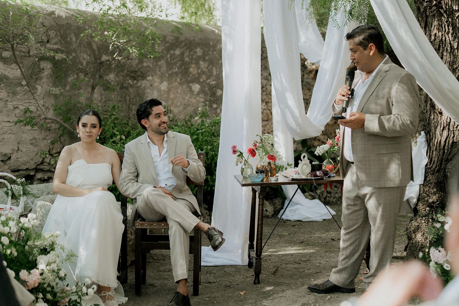 Outdoor wedding ceremony with white drapes and floral decorations in a natural garden setting.