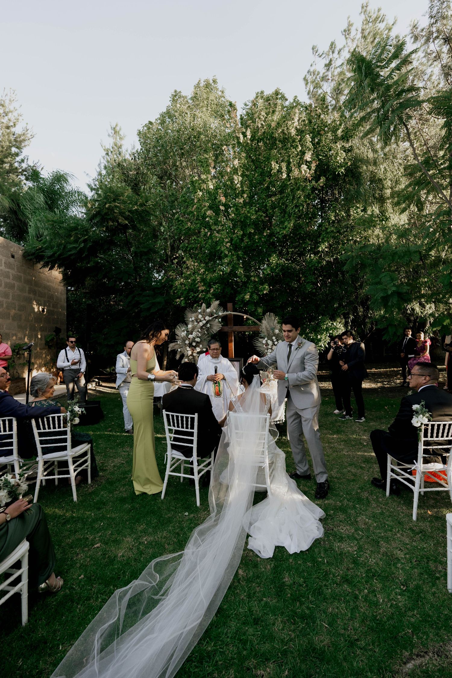 Elegant outdoor wedding ceremony with white chairs and flowing bridal veil on grass.