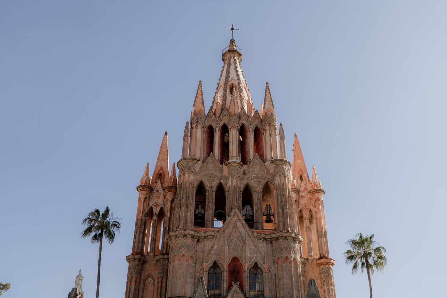 Gothic cathedral spires reach into a bright blue sky with palm trees visible.