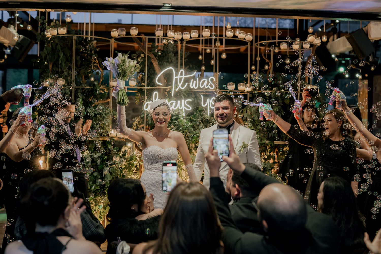 Festive crowd dances and celebrates under decorative lighting at an indoor venue.