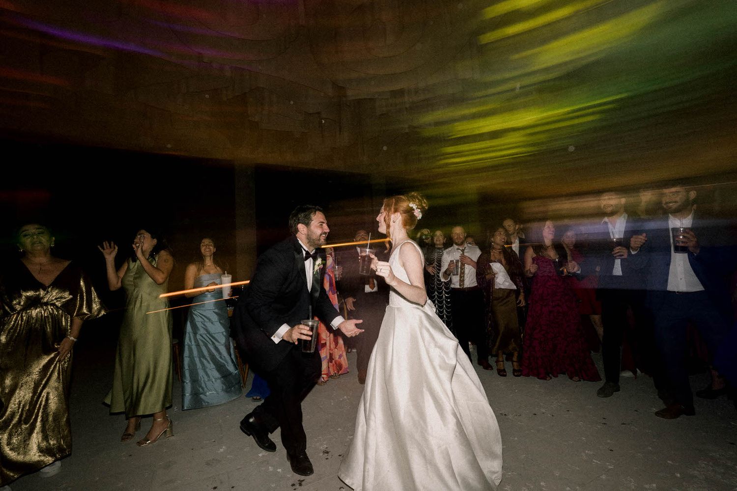 Wedding reception dance floor with guests celebrating under colored lights.