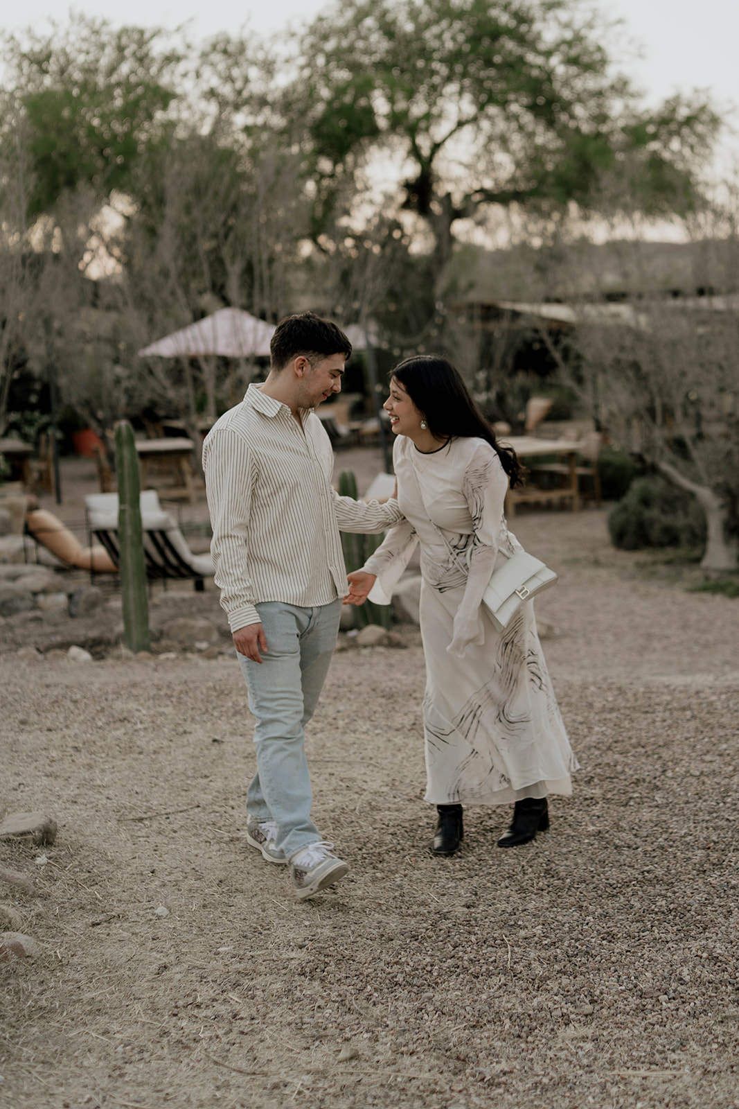 Two people in light colored outfits walking together on gravel path outdoors.