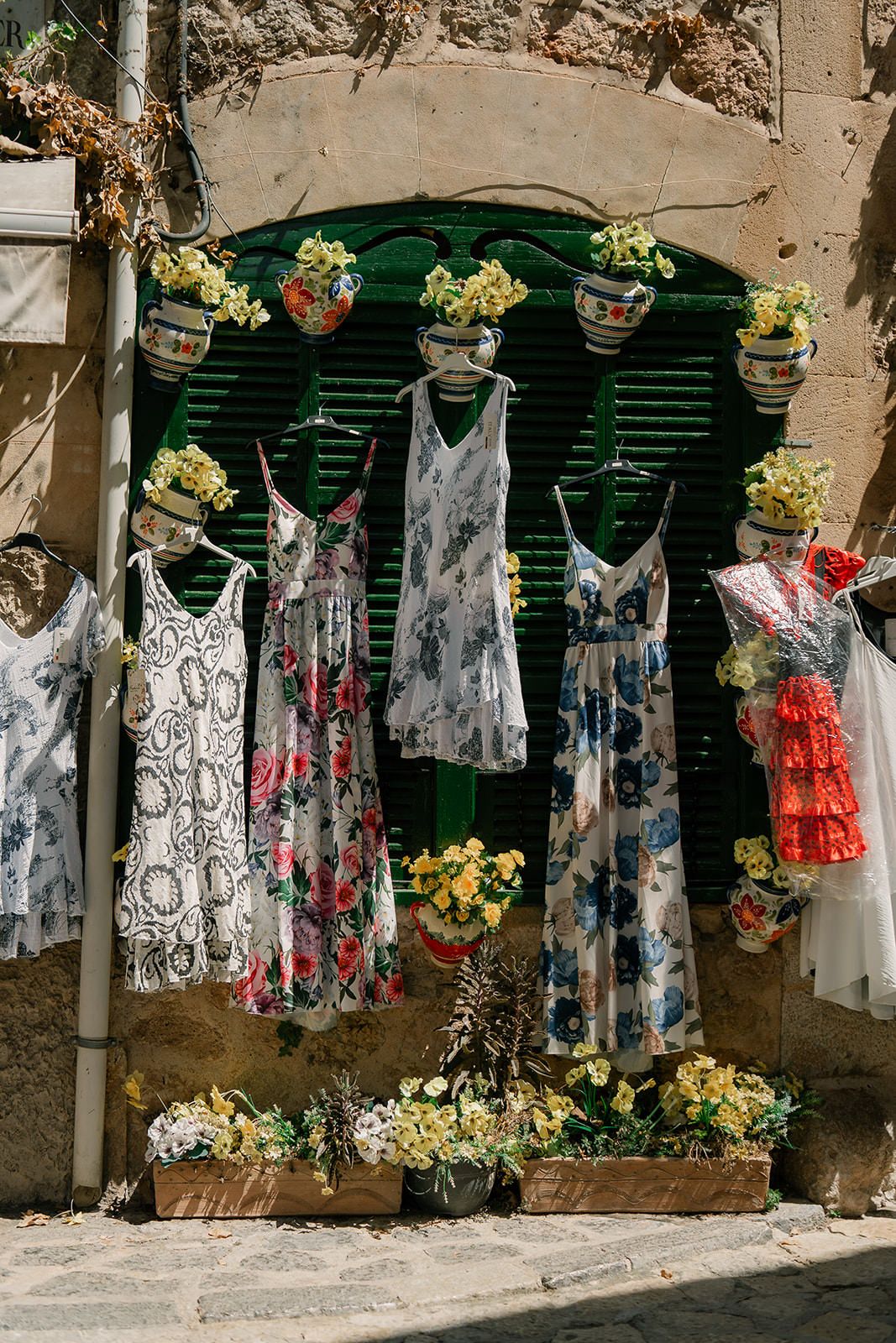 Colorful summer dresses and clothing items hanging on display outside a stone building.