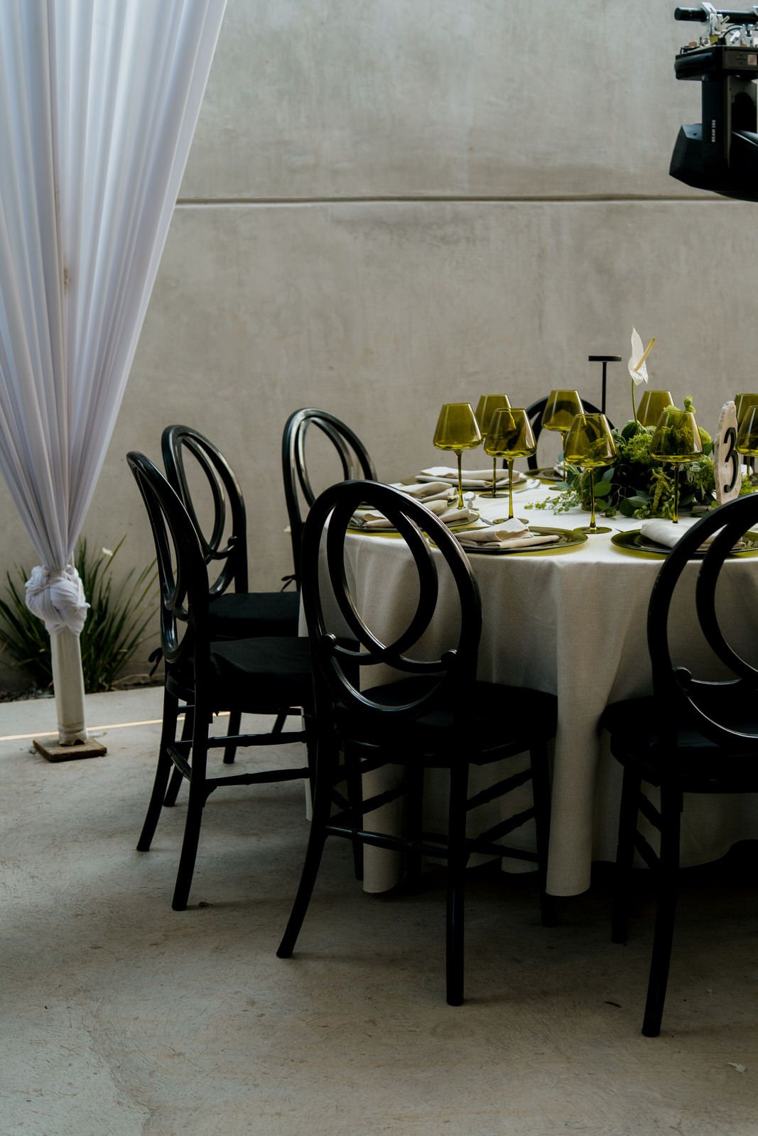 Black bentwood chairs surrounding a white-clothed table with green centerpieces and gold accents.