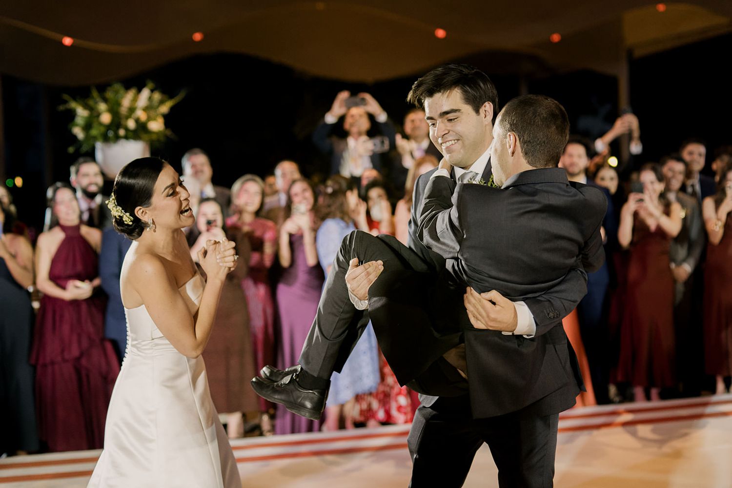 Bride and groom share a joyful first dance moment with groom lifted by a guest at wedding reception.