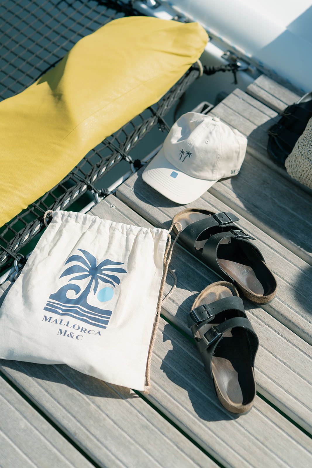 Beach accessories including sandals, a white tote bag with palm tree logo, and a yellow towel on wooden deck.