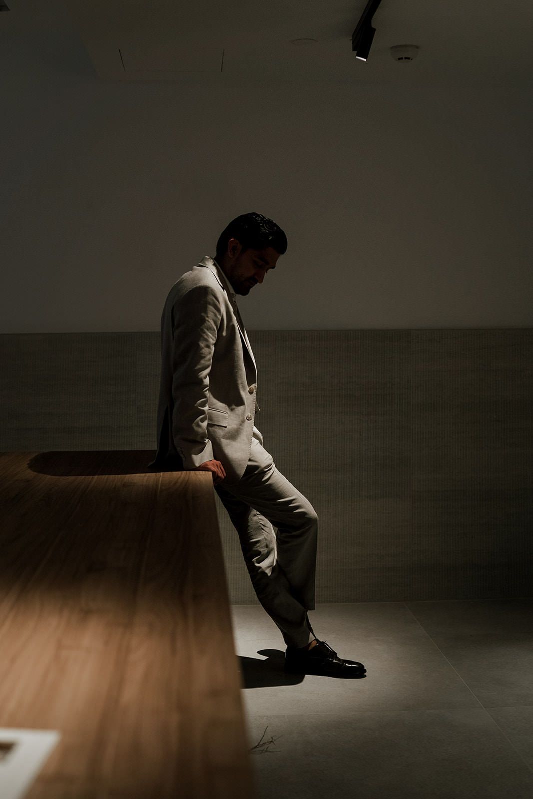 Person in gray sweater sits in dramatic moody lighting on wooden floor creating artistic silhouette effect.