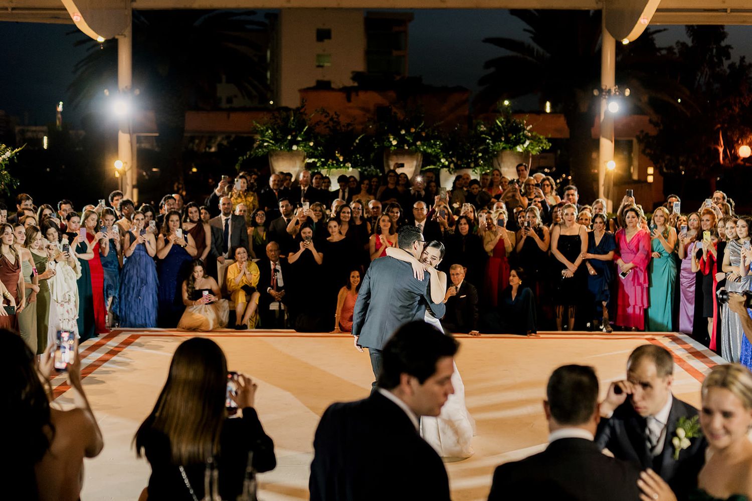 Large wedding reception crowd surrounding couple on outdoor dance floor at night.