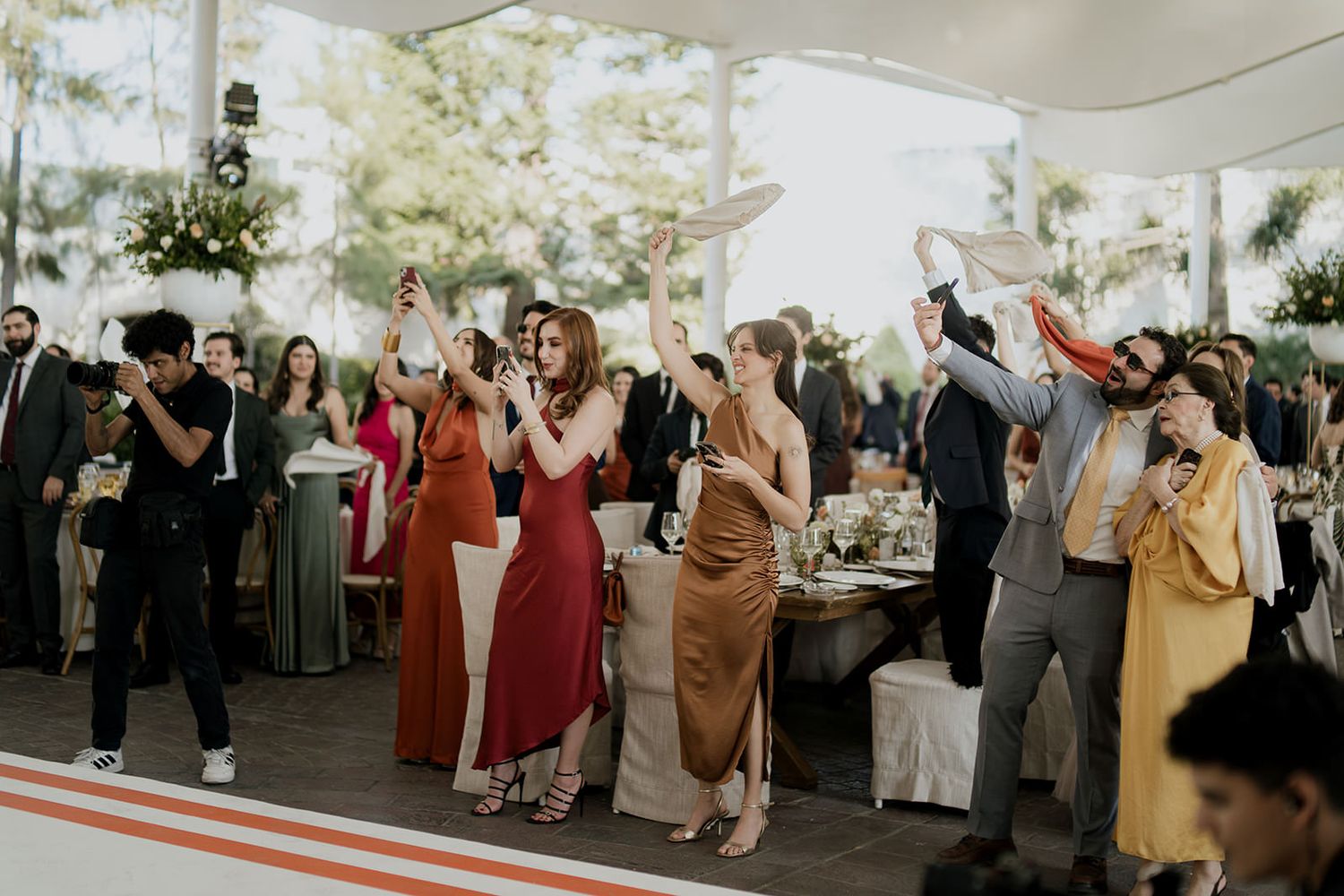 Guests in colorful formal attire celebrate at an elegant outdoor wedding reception under a white tent.