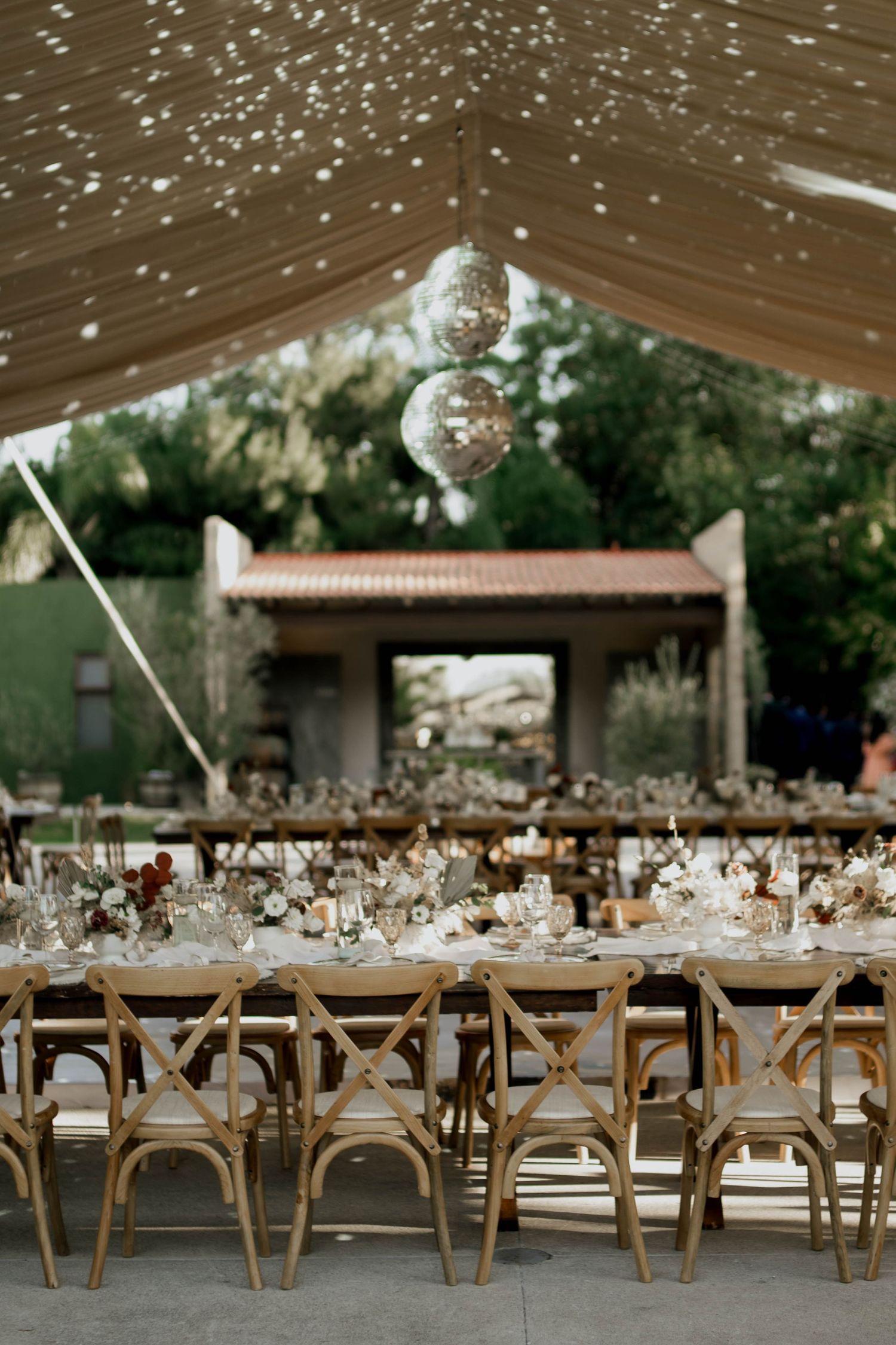 Reception tables set with elegant place settings under a tent with hanging disco balls.