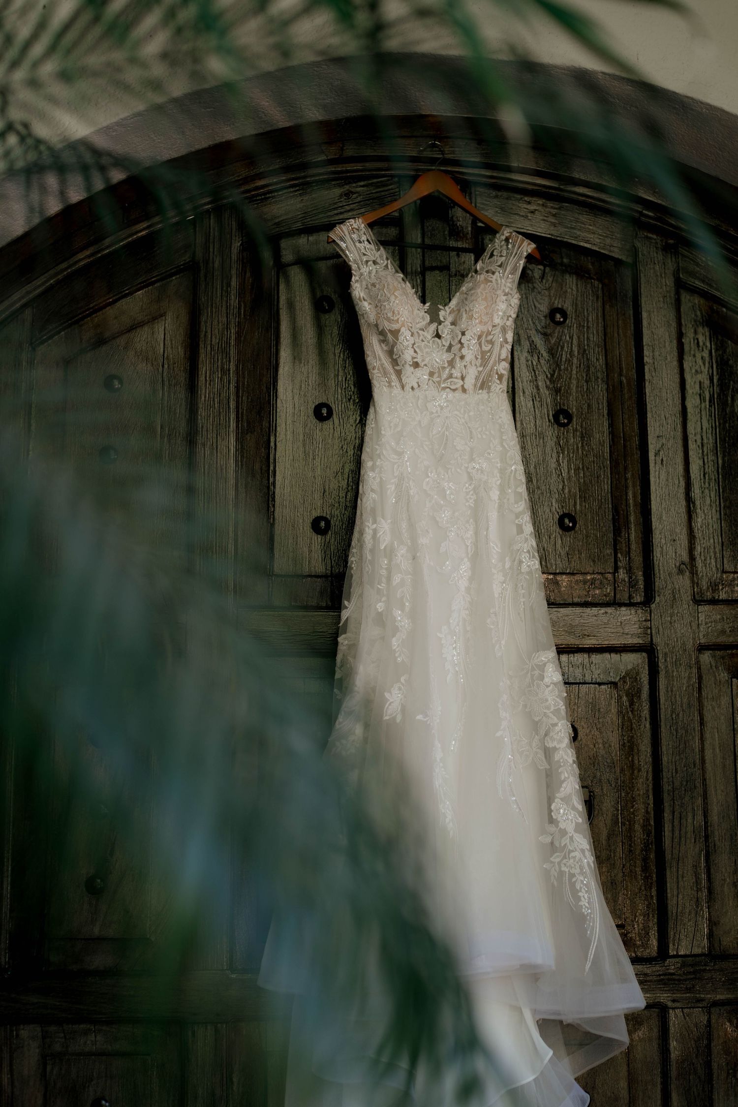 An elegant lace wedding gown displayed against a vintage wooden door with natural lighting.
